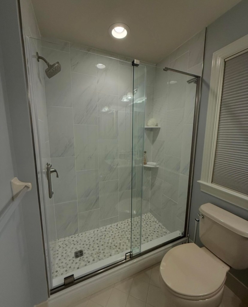 Walk-in shower with a frameless glass door and pebble tile floor